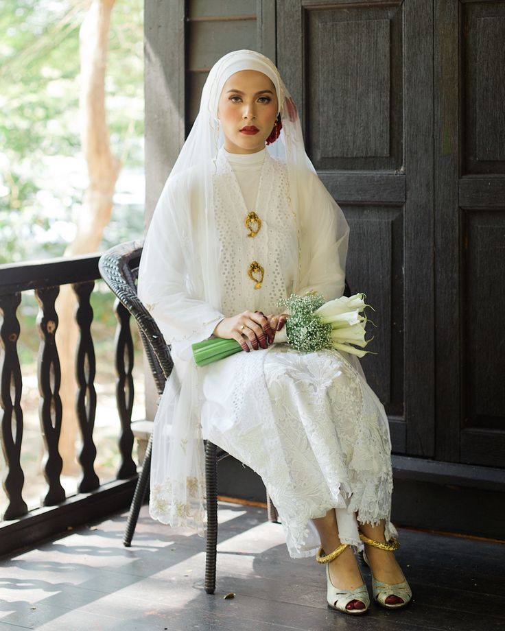 a woman sitting on a chair wearing a white dress and holding flowers in her hand