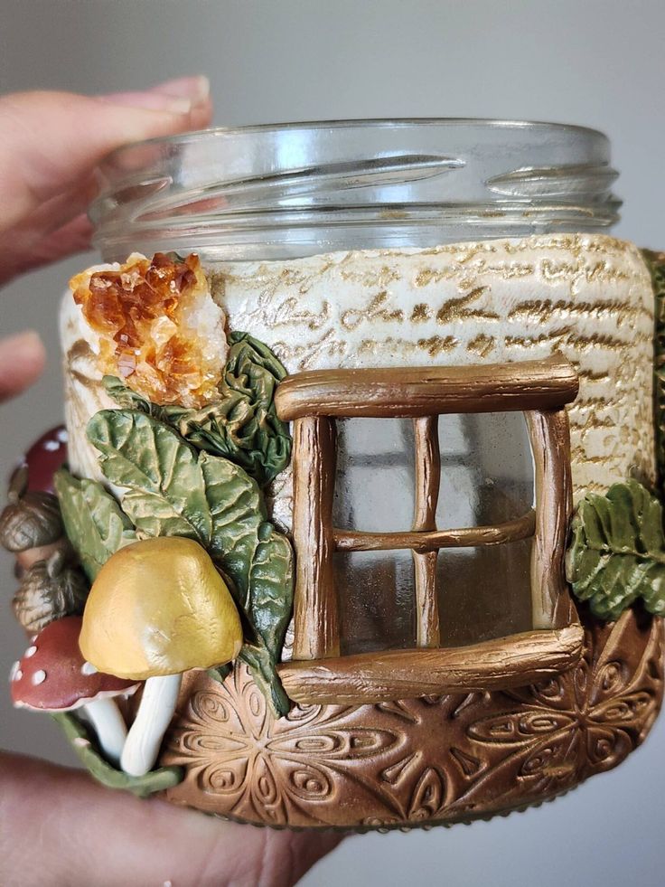 a hand holding a glass jar filled with miniature items like mushrooms, leaves and a window