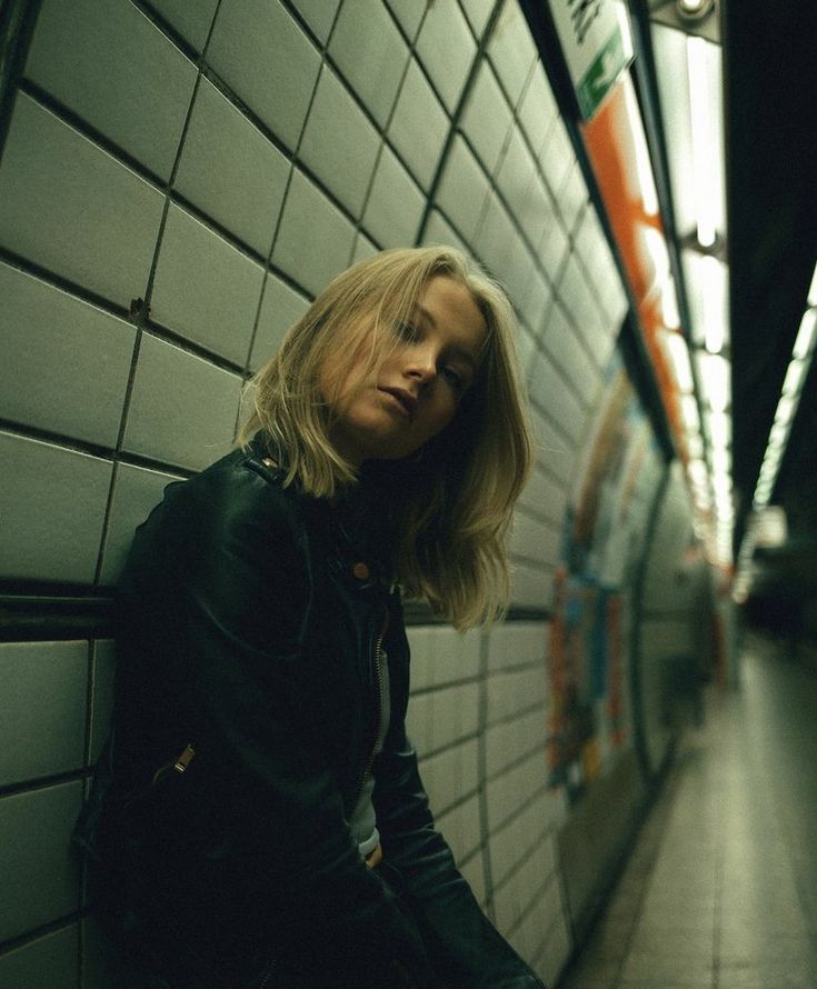 a woman leaning against a wall in a subway station