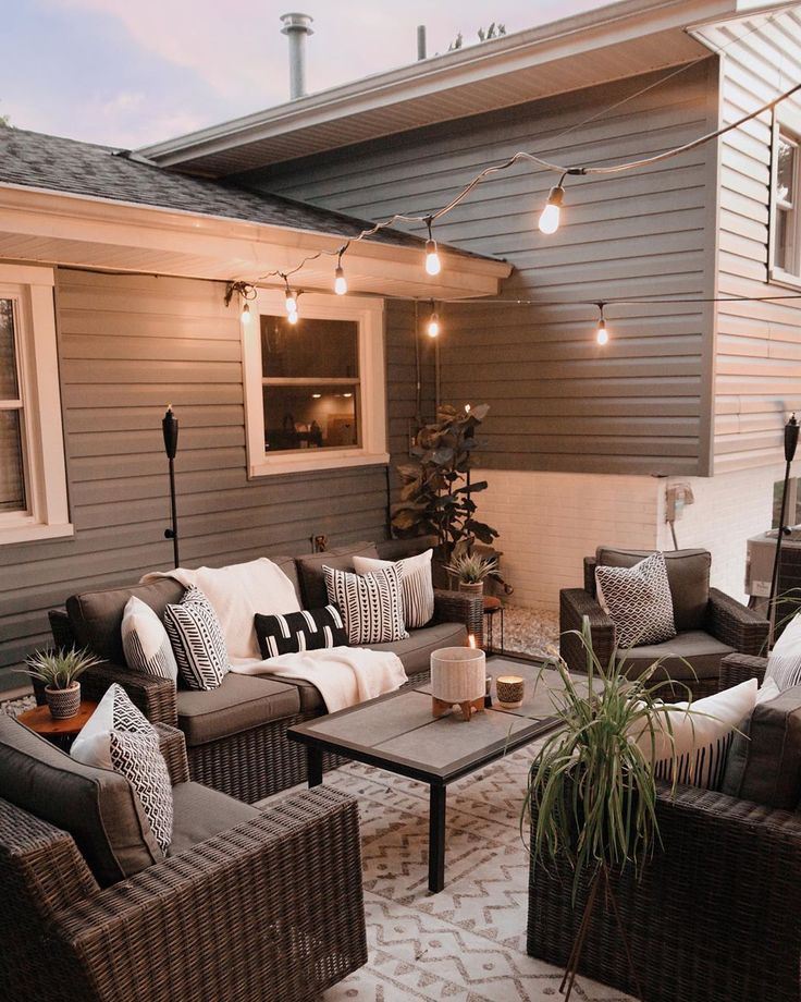 an outdoor living area with wicker furniture and string lights on the side of the house