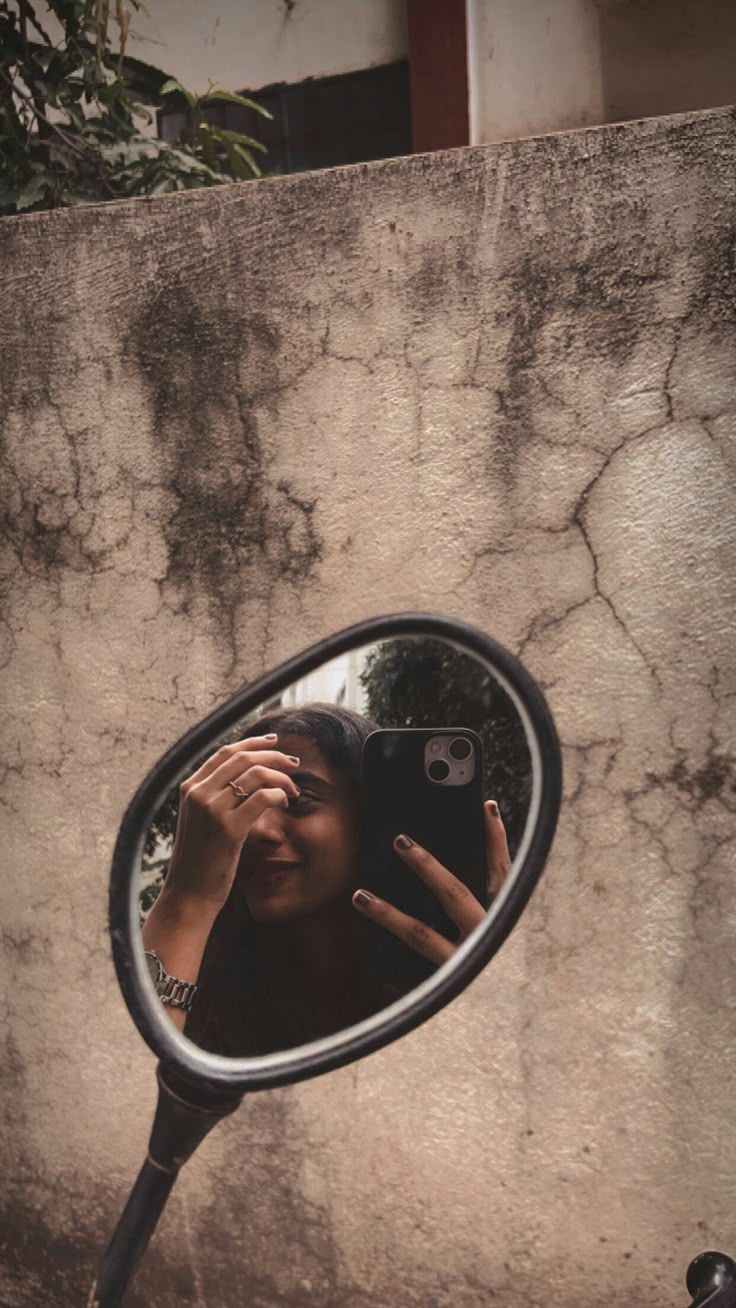 a woman taking a selfie in the side mirror of a motorcycle with her hand up to her face