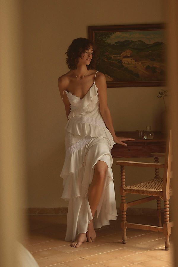 a woman in a white dress sitting at a table with a painting on the wall behind her