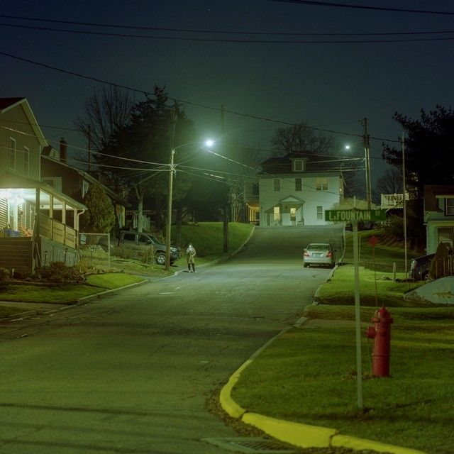 an empty street at night with cars parked on the side and houses in the background