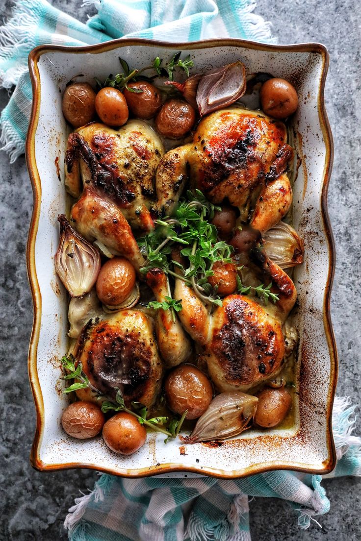 roasted chicken with garlic and herbs in a square dish on a blue towel, top view