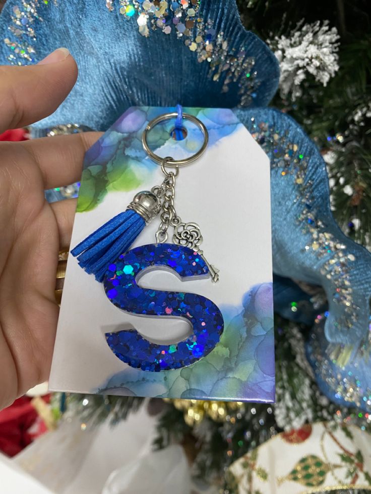 a hand holding a keychain with the letter s on it and a blue tassel