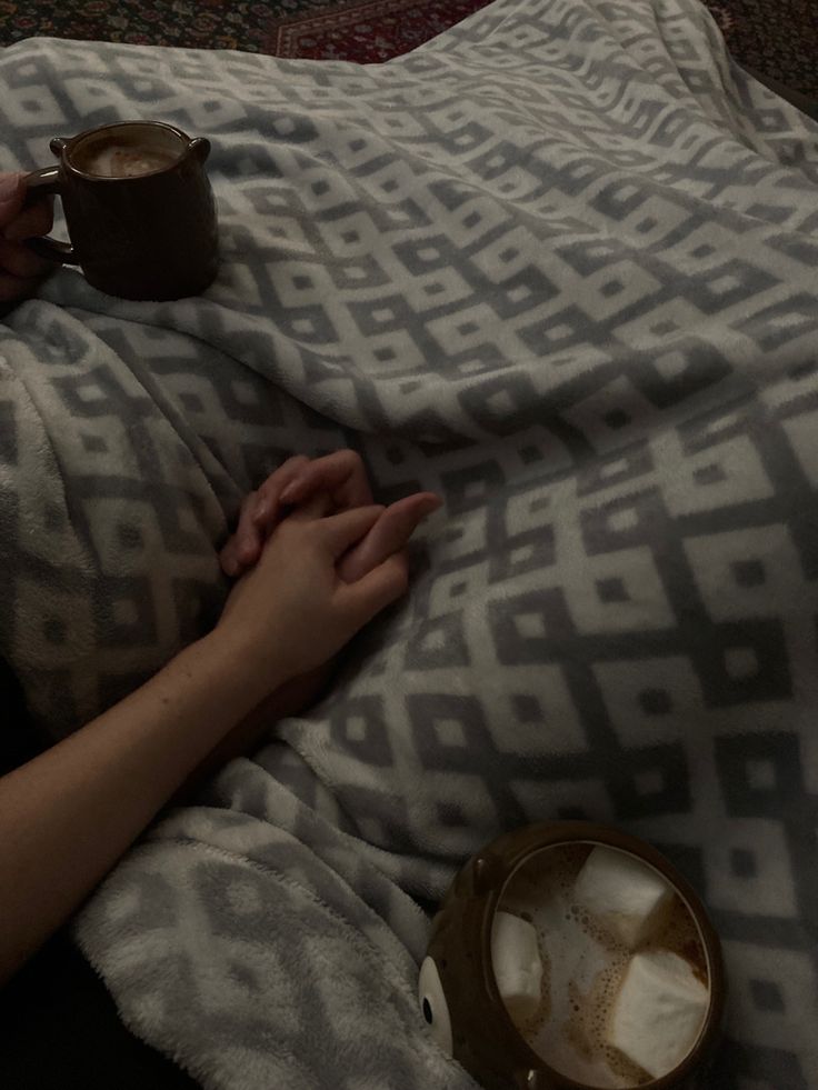 a person laying in bed with a cup of coffee on top of their stomach and blanket