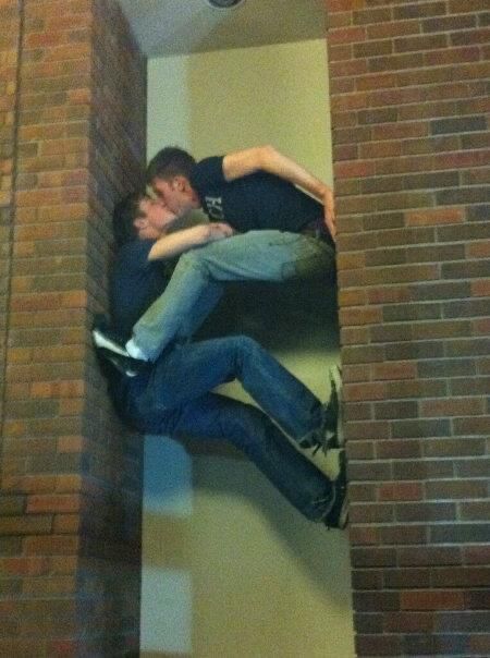 two young men are hanging upside down on a brick wall, one is holding the other's head