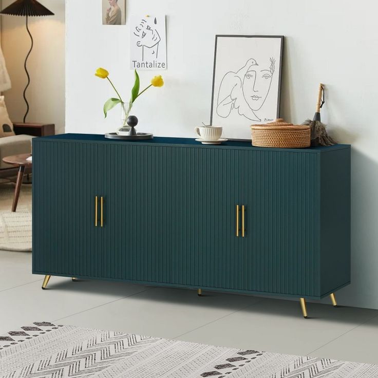 a green cabinet with brass legs in a room next to a rug and pictures on the wall