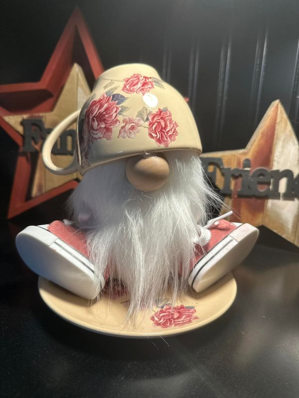 a gnome with white hair wearing a flowered hat and pink tennis shoes sits on a saucer