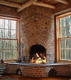 a brick fireplace in the corner of a room with two large windows and wood flooring