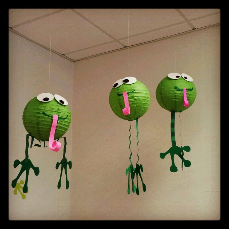 three green paper lanterns with faces and mouths hanging from the ceiling in an office cubicle