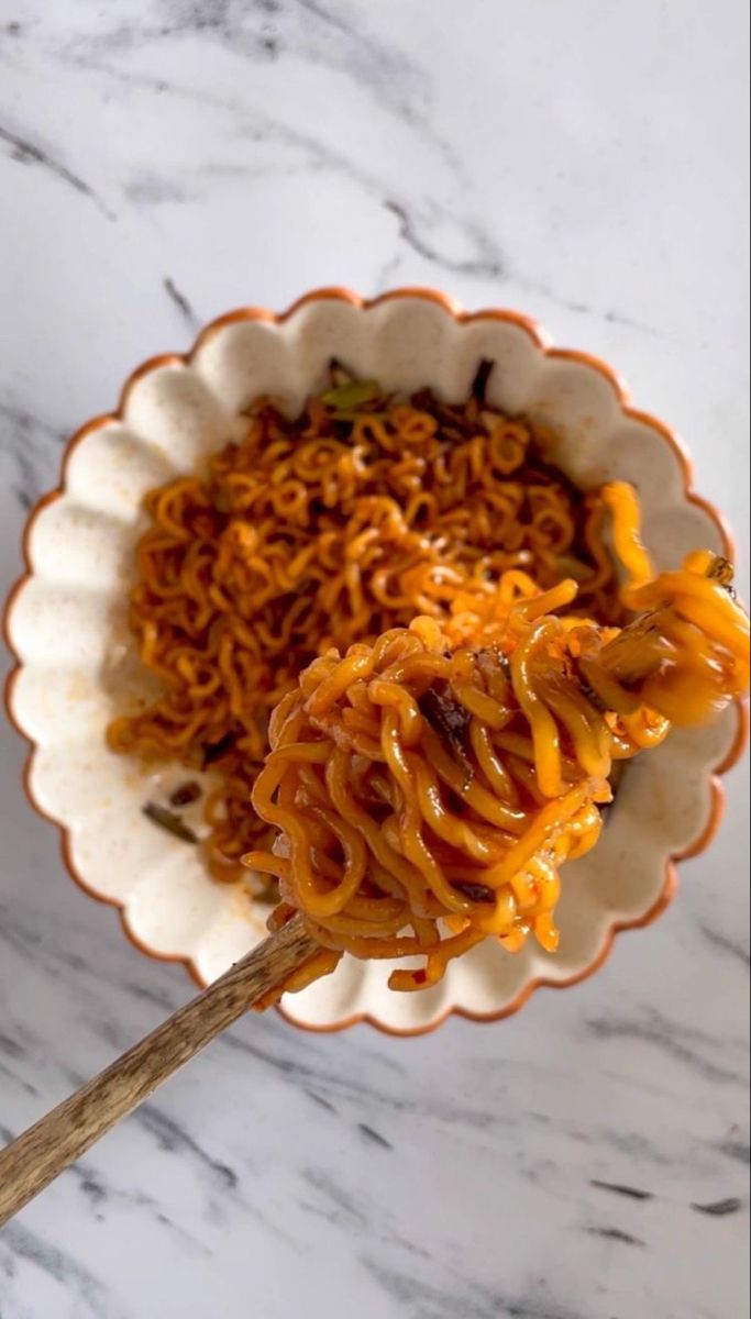 a bowl filled with noodles and sauce on top of a marble countertop next to a wooden spoon