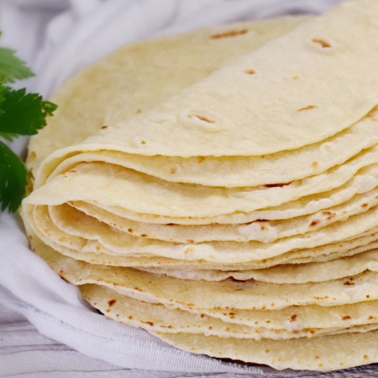 a stack of tortillas sitting on top of a white cloth next to parsley