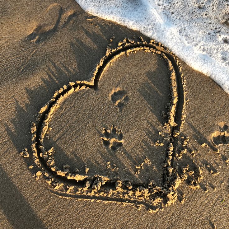 a heart drawn in the sand next to the ocean shore with footprints coming out from it