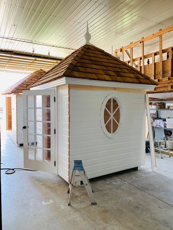 a small white building with a brown roof and window on the side, in a garage