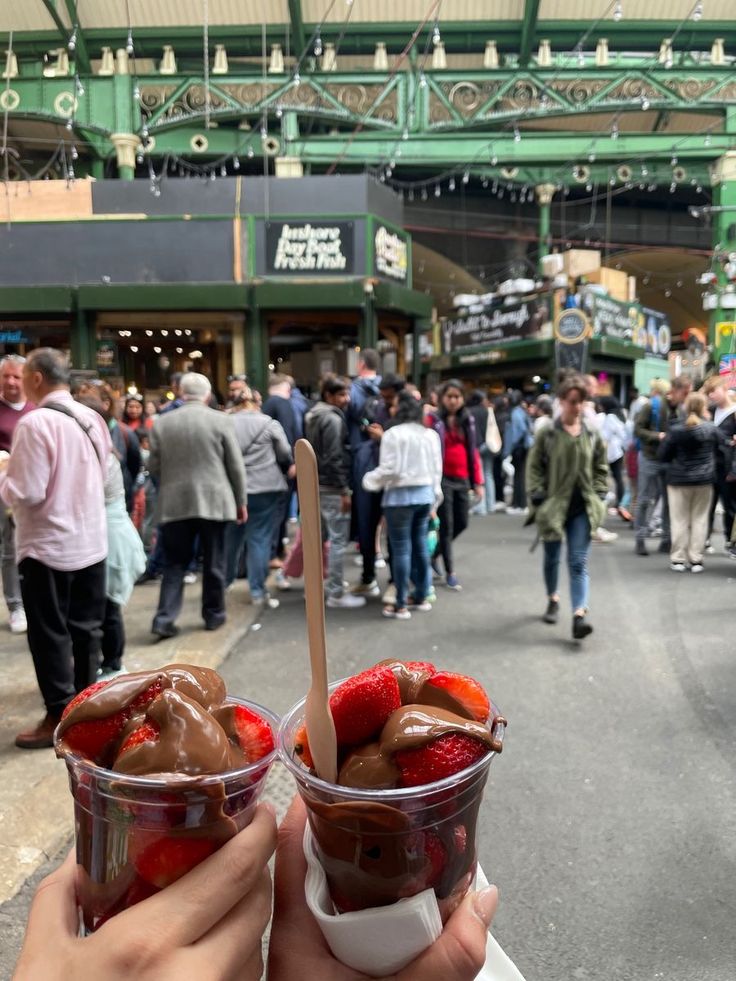 a person holding up two cups filled with ice cream and strawberries in front of a crowd