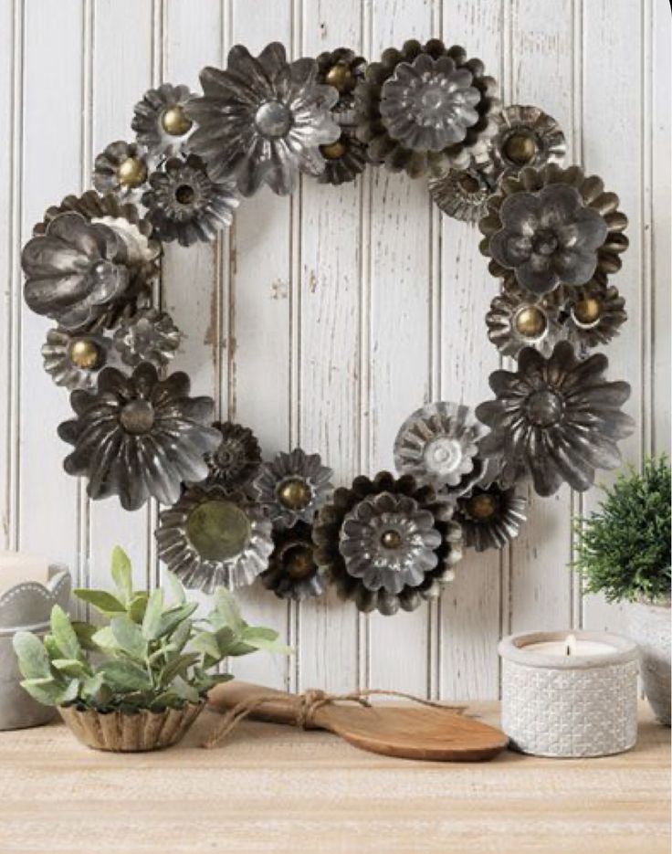 a wreath made out of metal flowers sitting on top of a wooden table next to a potted plant