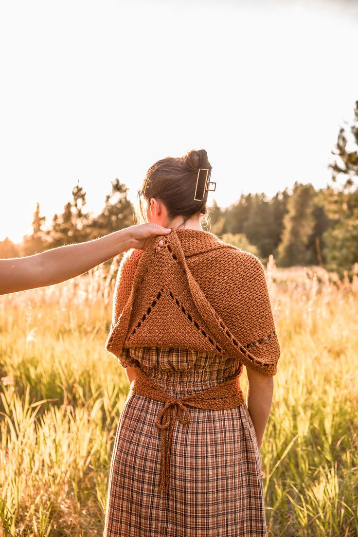 a woman standing in a field with her back to the camera, wearing a brown sweater and plaid skirt