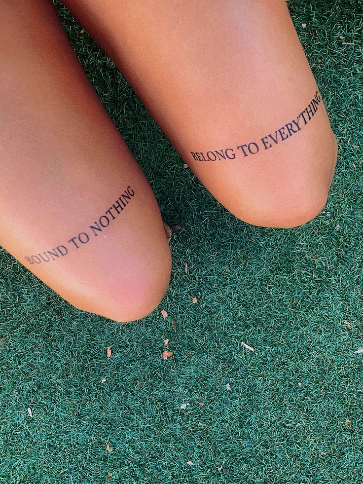 two feet with words written on them sitting in the grass next to a teddy bear