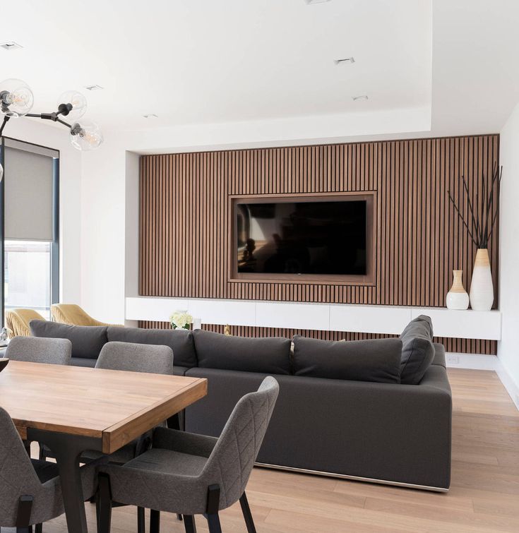 a modern living room with wood paneling and gray couches in front of a flat screen tv mounted on the wall