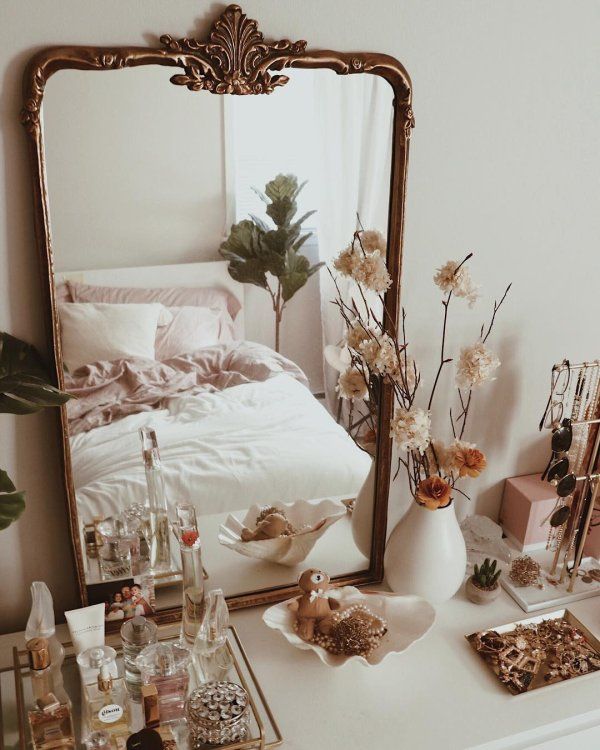 a mirror sitting on top of a white dresser next to a vase filled with flowers