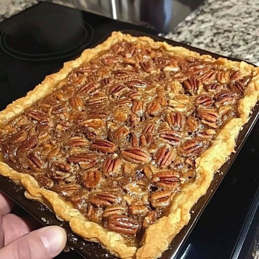 a person holding up a pecan pie in front of a stove top with the oven door open