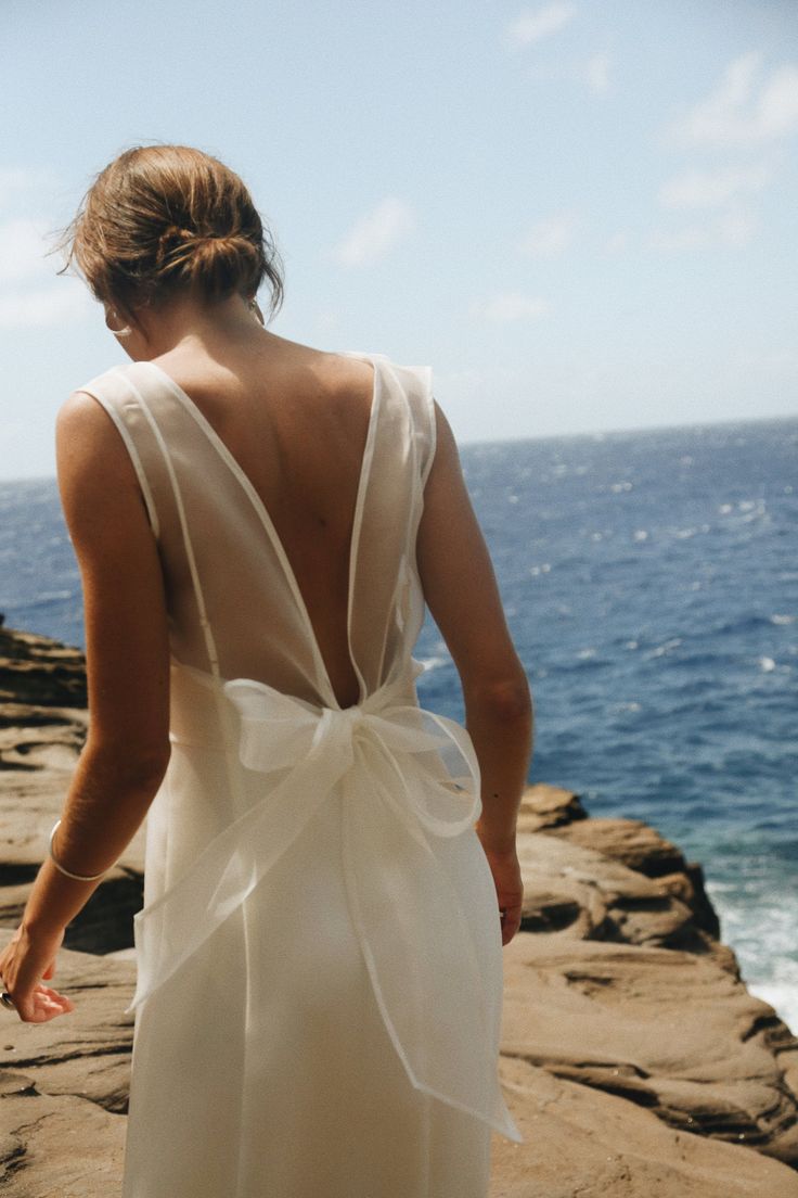 a woman standing on top of a rocky cliff next to the ocean wearing a white dress