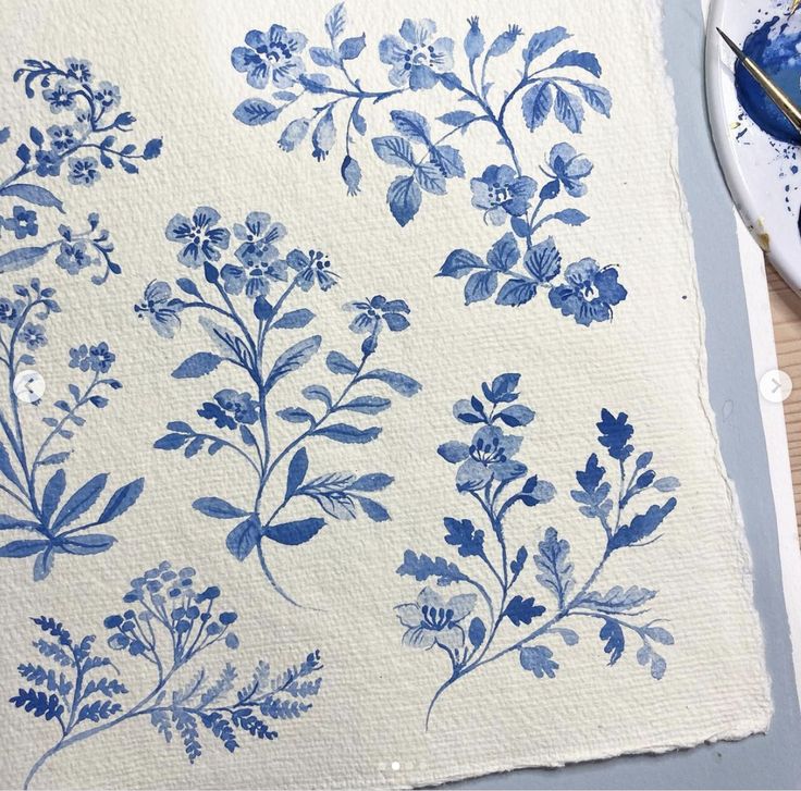 blue and white flowers are on a piece of paper next to some paintbrushes