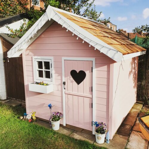 a small pink shed with a heart on the window and flowers in pots next to it