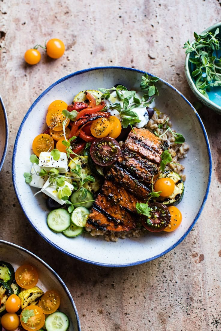 three bowls filled with different types of food on top of a wooden table next to oranges and cucumbers