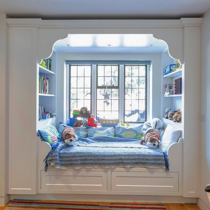 a child's bedroom with stuffed animals on the bed and bookshelves in the window