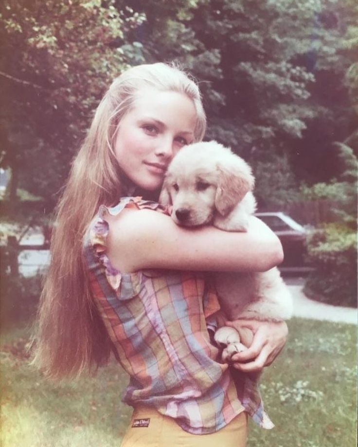 a young woman holding a puppy in her arms and looking at the camera while standing outside