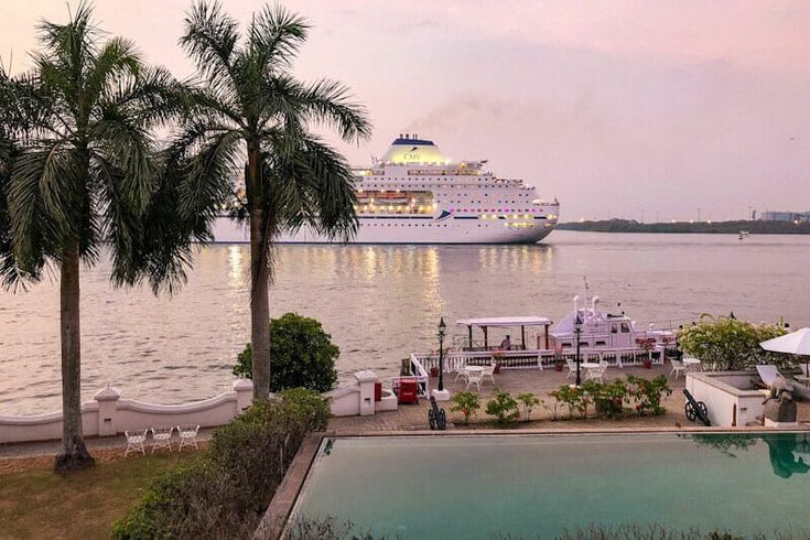 a cruise ship is docked in the water next to some palm trees and tables with umbrellas