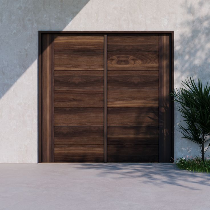 a large wooden garage door sitting in front of a white building with a plant next to it