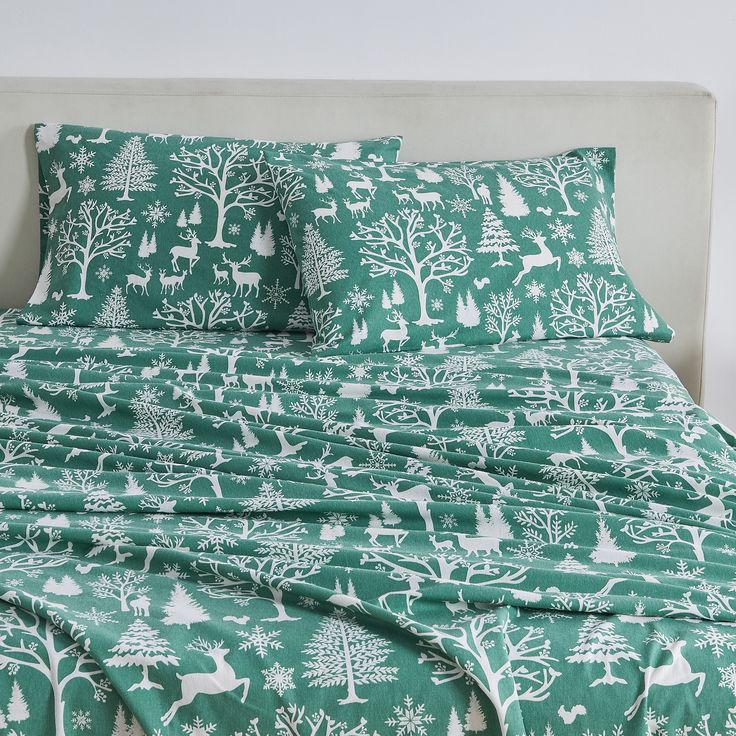 a bed covered in green and white christmas themed sheets with deer, trees, and snowflakes on them