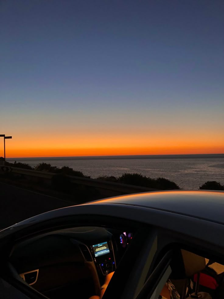 the sun is setting over the ocean as seen from inside a car with its dashboard up