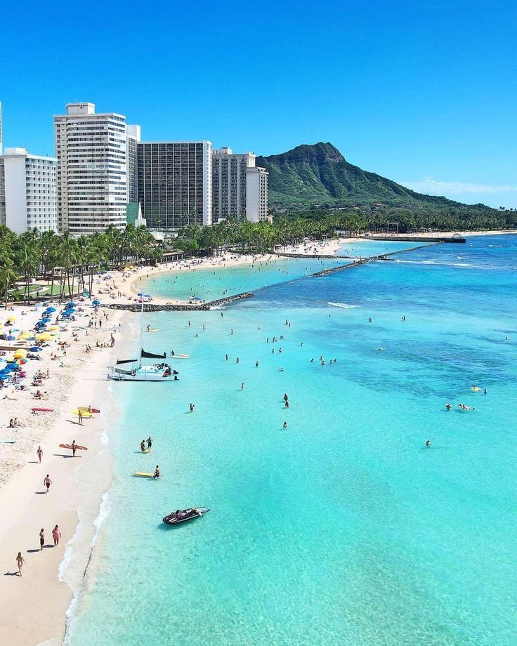 people are on the beach and in the water near buildings with umbrellas over them