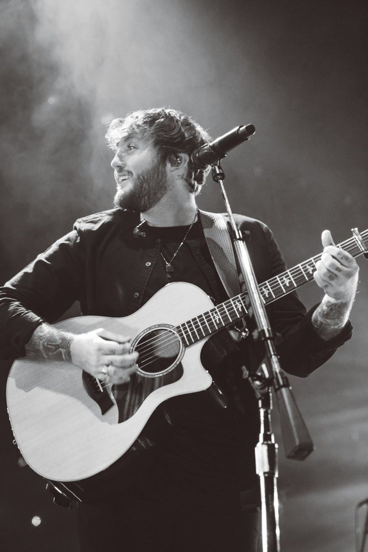 a man holding a guitar while standing in front of a microphone on top of a stage