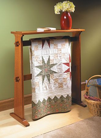 a wooden stand with a quilt hanging from it's sides and a basket on the floor next to it