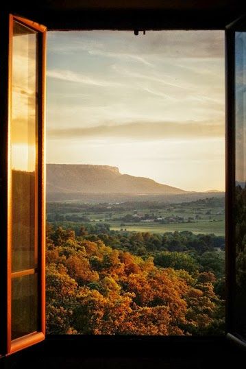 an open window shows the view of mountains and trees from inside a room with large windows