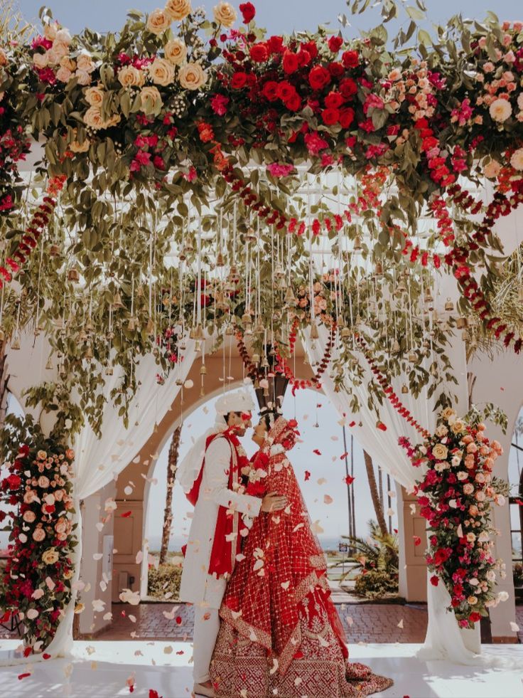 a bride and groom standing under an archway decorated with red, white and pink flowers