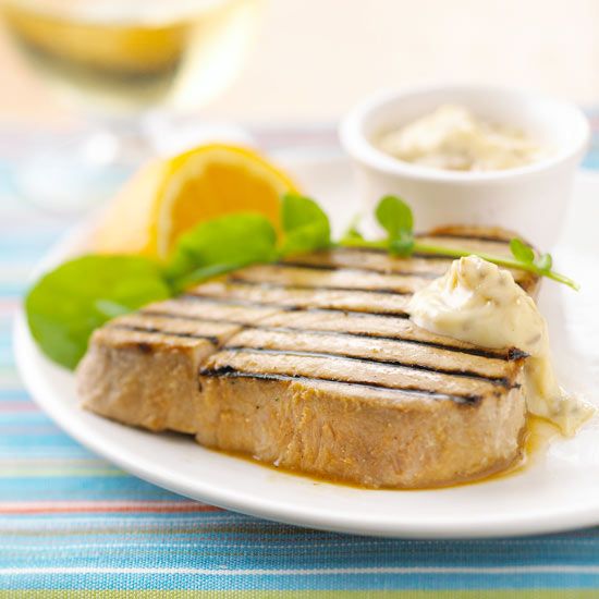 a grilled steak on a white plate with garnish and lemon wedges