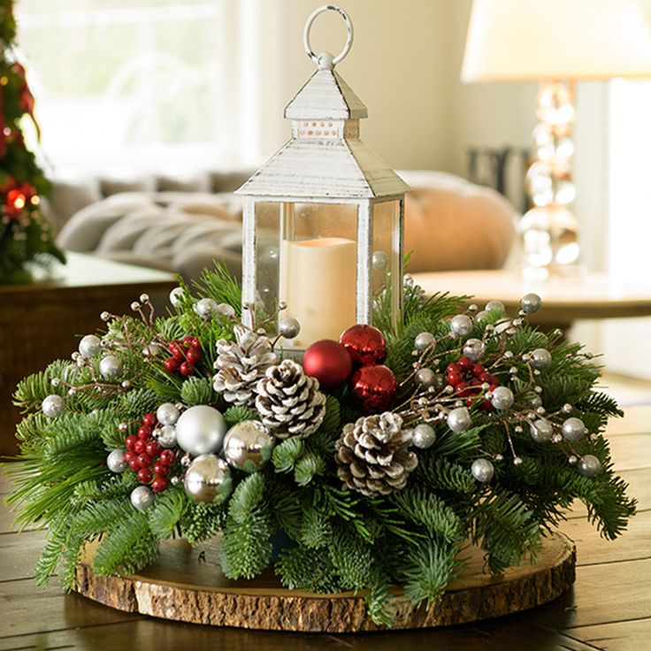 A holiday centerpiece of noble fir, white pine, incense cedar, silver glittery bead decorations, 2 red ball clusters, 2 silver ball clusters, 6 red berry clusters, 6 Australian pinecones with silver glitter, and an LED white lantern sitting on a wood round on a table up close. Dining Table Candle Decor, Christmas Tree Centerpieces For Table, Table Candle Decor, Christmas Lantern Centerpieces, Dining Table Candle, Frosted Pinecones, Holiday Centerpieces Christmas, Red Ball Ornaments, Winter Centerpiece