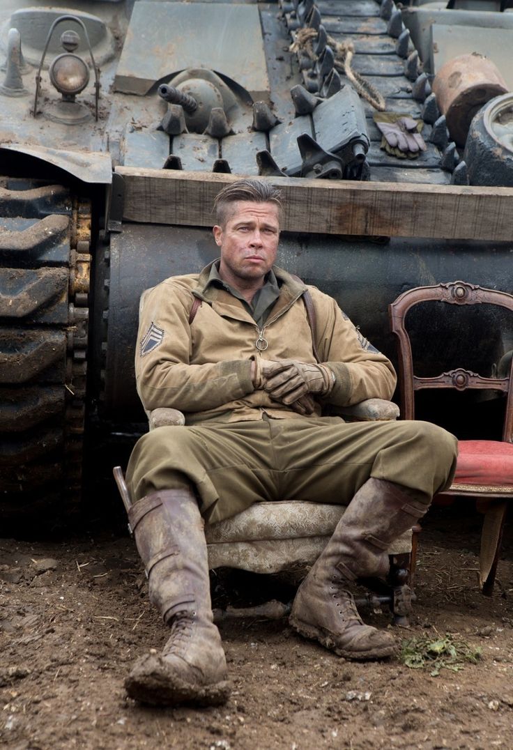 a man sitting on top of a chair in front of a tank with rusted tires