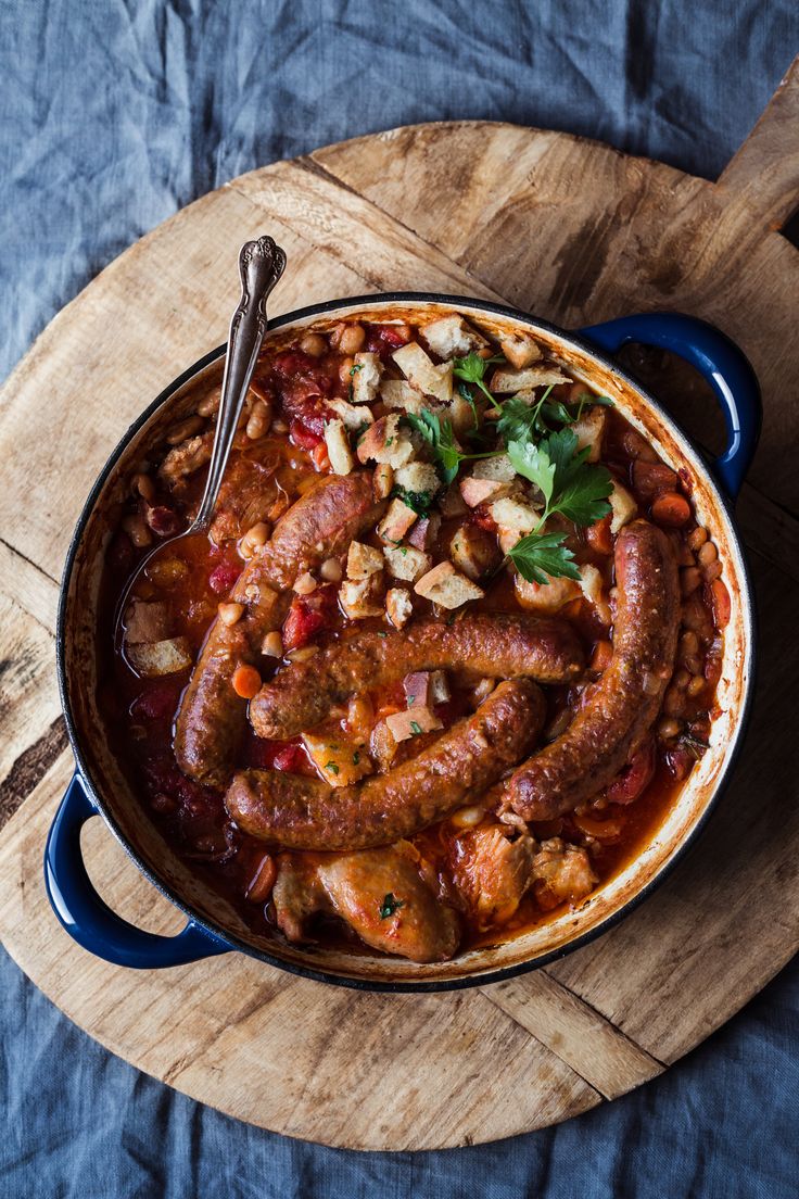 a blue pot filled with lots of food on top of a wooden cutting board next to a spoon