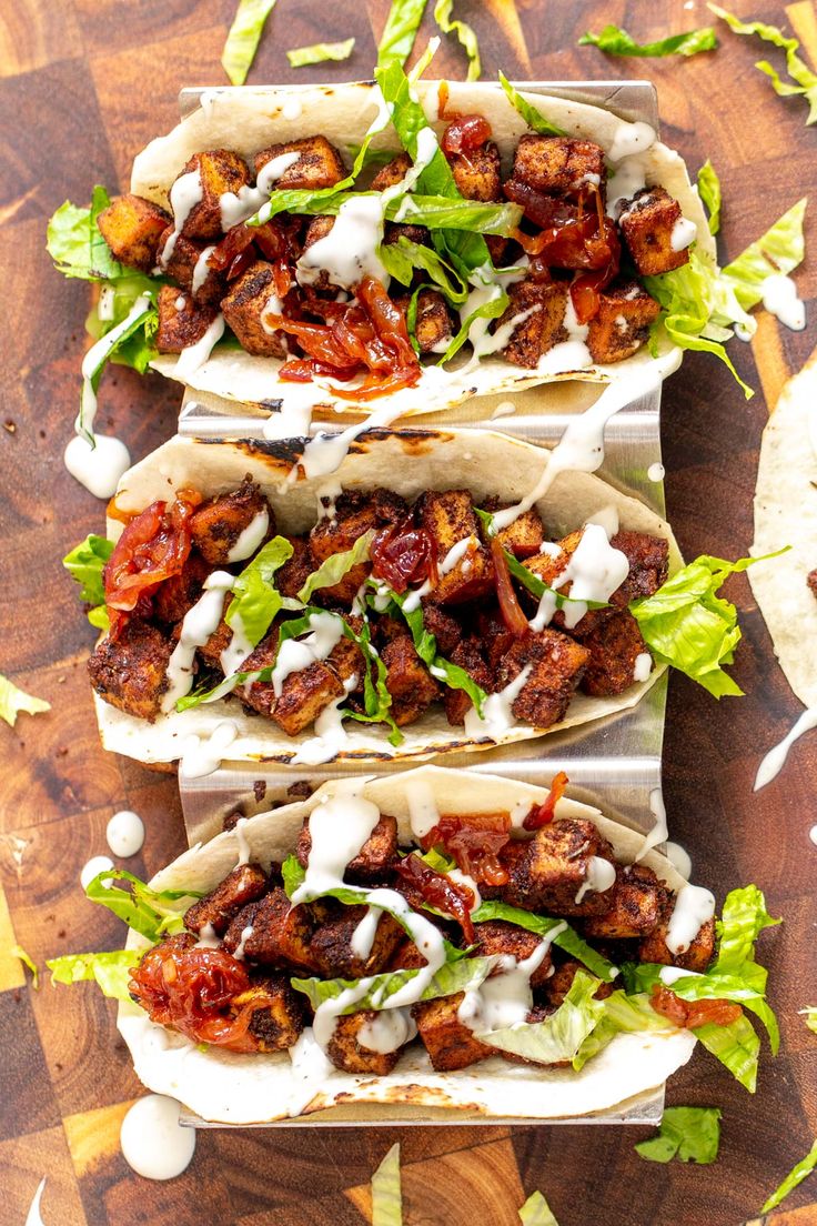 three tacos filled with meat and lettuce on top of a wooden cutting board