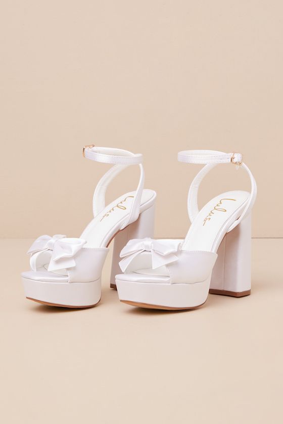 Your walk down the aisle just got even more fabulous, thanks to the Lulus Pearlla Bow White Satin Platform High Heel Sandals! These sleek satin heels feature a trendy square toe upper (atop a 1"" toe platform), and a wide toe strap adorned with a darling bow detail. Matching straps sprout from the sides to wrap and secure around the ankle with a gold buckle, all atop a sky-high block heel that is sure to take your look to the next level! 4. 5" wrapped block heel. Cushioned insole. Felted rubber White High Heels For Quinceanera, White Wedges Heels, White Shoes With Bow, High Heels For Graduation, Confirmation Heels, White Heels Simple, Formal Heels Classy, Plain White Heels, White Hoco Heels