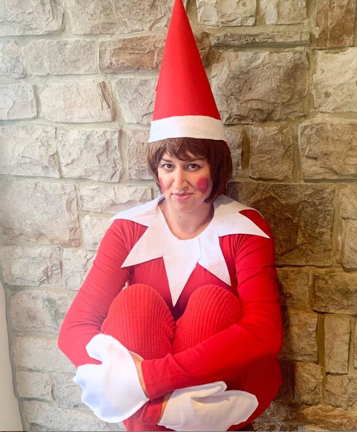 a woman dressed in an elf costume standing next to a brick wall with her arms crossed