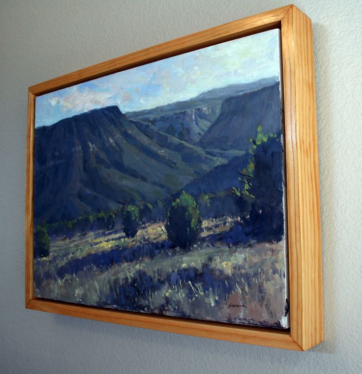 a painting hanging on the wall in a room with a white wall and wooden frame