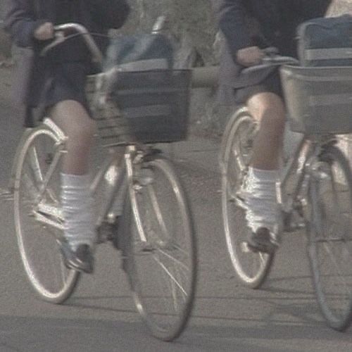 two people riding bikes with baskets on the front and back wheels, one person wearing white socks